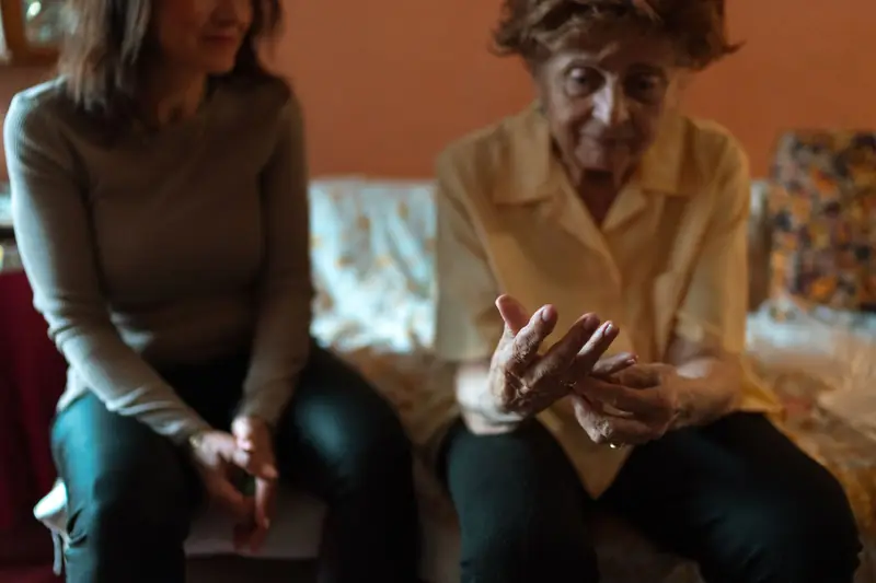 An older woman talks with her caregiver on a living room couch at home