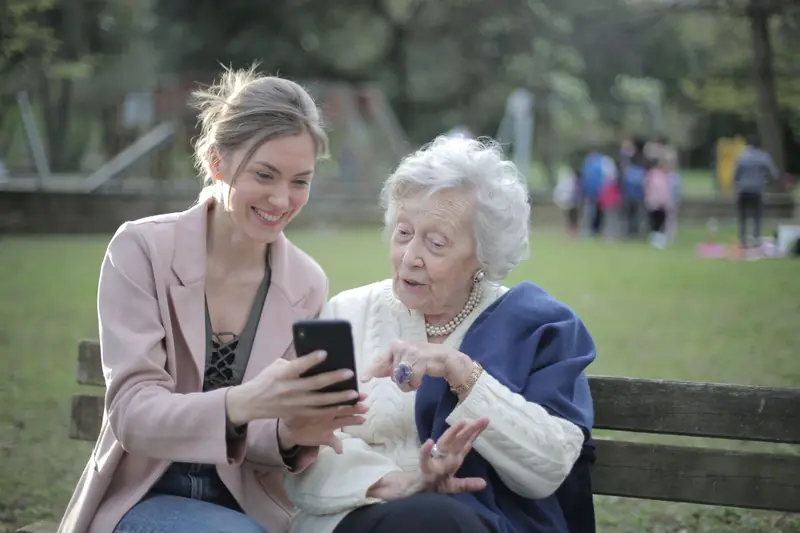 A young woman shows her grandmother something on a smartphone on a park bench